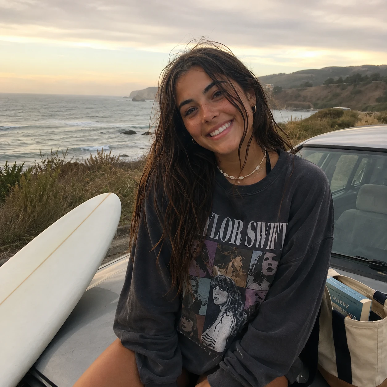 19-year-old woman with damp dark hair sitting by her surfboard on the Northern California coast.