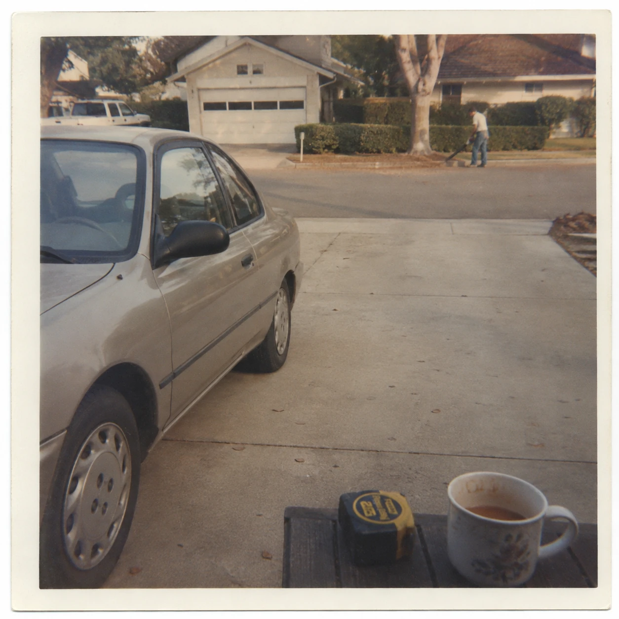 A modest Japanese car on a surprisingly spacious driveway in Silverdale, with Marcel’s tape measure and half-finished coffee in the foreground while a neighbour blows leaves across the street.